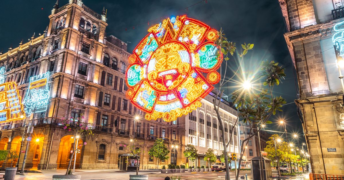 Nighttime view of a brightly lit downtown area in Mexico City, featuring traditional architecture and colorful lights.