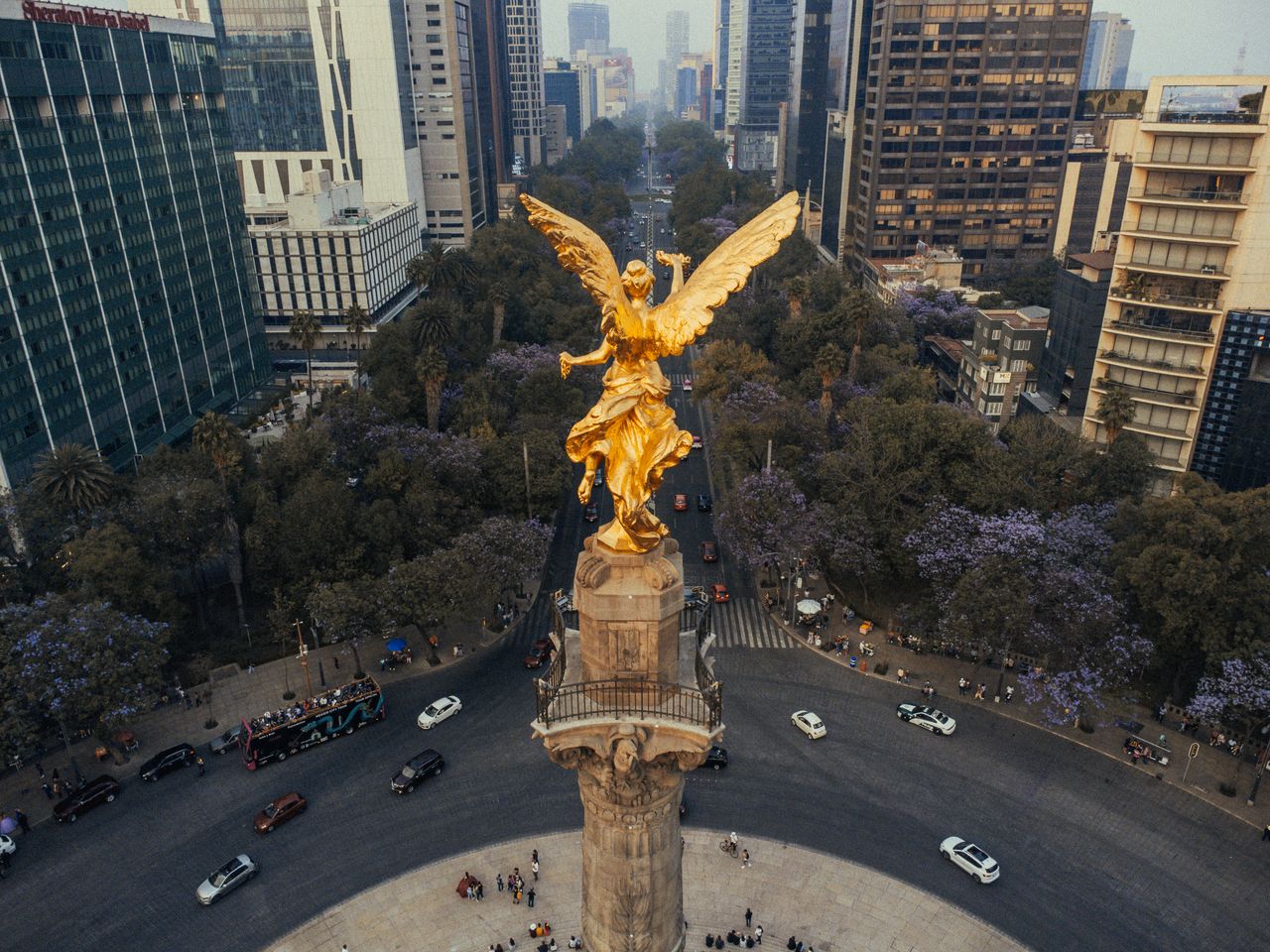 Drone shot capturing the Angel of Independence monument amidst bustling cityscape in Mexico City.