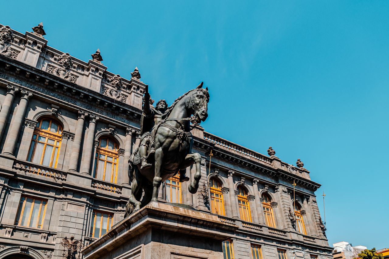 Low angle view of an equestrian statue in front of a historic building in Mexico City under clear blue sky.