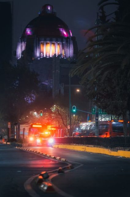 Vibrant nighttime scene of bustling city street with the illuminated Monumento a la Revolución in Mexico City.